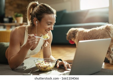 Happy sportswoman eating salad and having fun while using laptop at home. - Shutterstock ID 1661104066