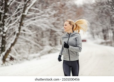 Happy sportswoman jogging on snowy path in woods at winter. Healthy lifestyle, winter fitness - Powered by Shutterstock