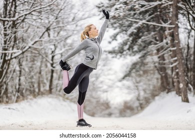 Happy Sportswoman Standing On Snowy Path At Winter And Stretching Her Leg. Warmup Exercises, Winter Fitness