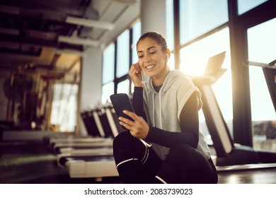 Happy Sportswoman Using Mobile Phone While Relaxing After Sports Training In A Gym. Copy Space.