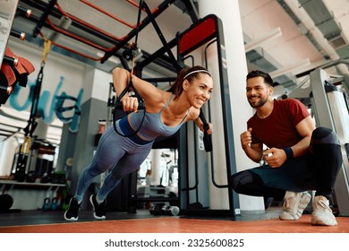 Happy sportswoman using suspension straps while exercising strength with coach's support in a gym. - Powered by Shutterstock