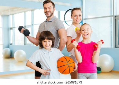 Happy and sporty. Happy family holding different sports equipment while standing close to each other in health club 