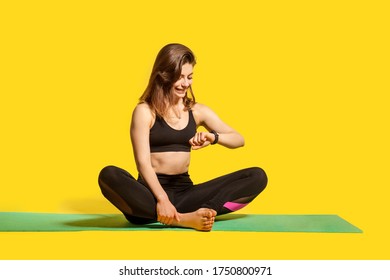 Happy sporty girl in tight sportswear sitting on gym mat, looking time, checking pulse in fitness tracker, using smartwatch to monitor heart beat, wearable app. Healthy lifestyle, isolated studio shot - Powered by Shutterstock