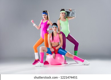 happy sporty girls with sports equipment and tape recorder on grey 