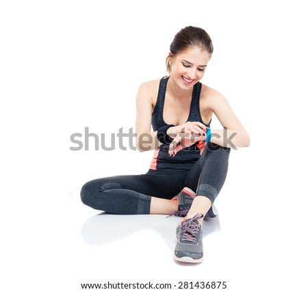 Happy sporty woman sitting on the floor and using smart watch isolated on a white background