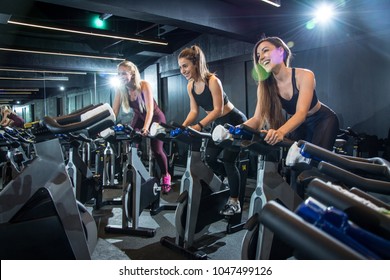 Happy Sporty Women Riding Exercise Bikes On Cycling Class In Gym.