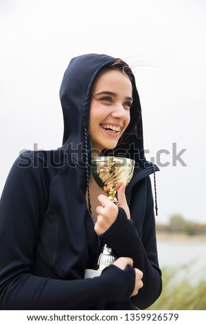 Happy sporty young woman holding gold trophy cup outdoor