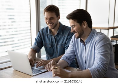 Happy startup partners using laptop and discussing project at workplace, making video call, watching virtual presentation, feeling joy about good teamwork result. Business coach teaching intern - Shutterstock ID 2161635145