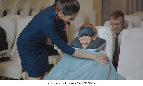 Happy stewardess taking care of passenger adult businesswoman, Air hostess or flight attendant woman covering tired sleepy elderly with blanket during trip on the airplane