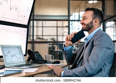 Happy Stock Broker Looking At Display, Smiling Wide, Holding Smartphone And Analyzing Dynamic On Forex Charts, Working In Office