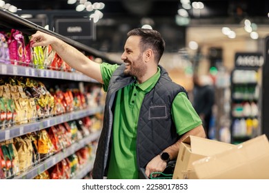 A happy stock clerk is arranging groceries on shelves at supermarket.