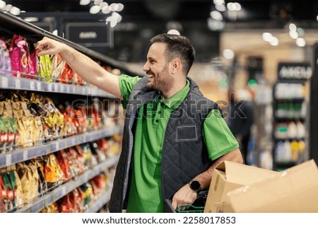 A happy stock clerk is arranging groceries on shelves at supermarket.