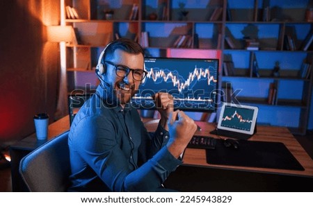 Happy stock trader is working by pc indoors and celebrating success. Conception of exchange and money.