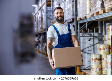 A happy storage worker in overalls with a tattoo on his arm is relocating a box with goods while walking in storage. The box is ready for shipping. - Powered by Shutterstock