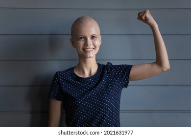 Happy strong cancer survivor beating disease, winning fight for life. Young woman with shaved head looking at camera, smiling, making power strength hand gesture. Head shot portrait