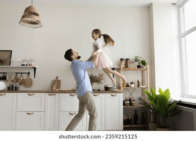 Happy strong dad playing active games with cheerful excited girl wearing pink girlish ballet skirt, lifting child up in air, dancing with kid training choreography, at home, laughing, having fun - Powered by Shutterstock