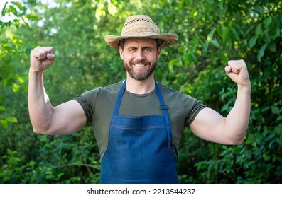 Happy Strong Farmer In Farmers Hat And Apron Flexing Arms On Farm Outdoors