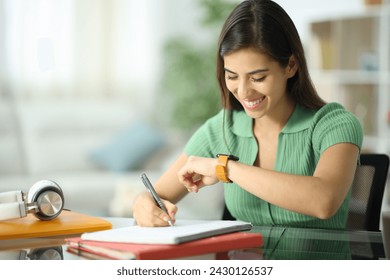 Happy student checking smartwatch taking notes at home - Powered by Shutterstock