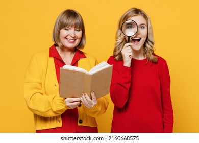 Happy Student Cool Woman 50s In Red Shirt Have Fun With Teenager Girl 12-13 Years Old. Grandmother Granddaughter Read Book With Magnifer Isolated On Plain Yellow Background. Family Lifestyle Concept