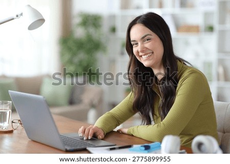 Happy student e-learning at home using laptop looks at camera
