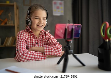 Happy Student Girl Wearing Headphones Studying Online At Home, Looking At Phone Screen, Engaged In Video Conference, Watching Webinar, Using Smartphone On Tripod, Homeschooling Concept