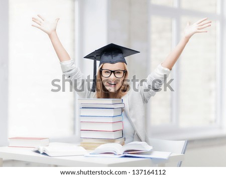 happy student in graduation cap with stack of books