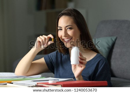 Happy student holding a vitamin pill studying late hours in the night at home