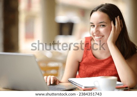 Happy student with notebook and laptop looks at you in a coffee shop terrace