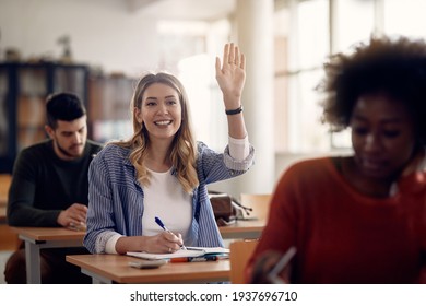 Happy student raising her arm to answer a question during a class at university classroom. 