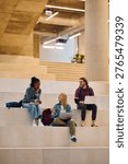 Happy student using laptop while talking to her friends at the university. Copy space.