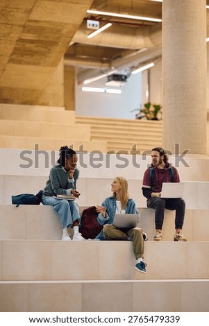 Happy student using laptop while talking to her friends at the university. Copy space.