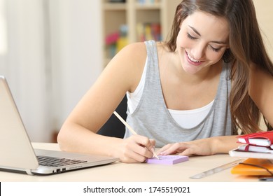 Happy Student Woman With Laptop Writing On Post Note Sitting On A Desk At Home