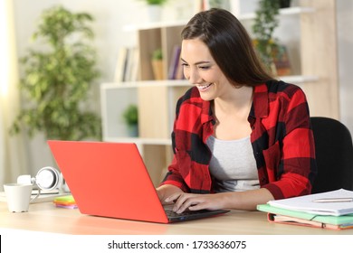 Happy student woman studying typing on red laptop sitting on a desk at home