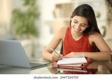 Happy student writing in a notebook sitting at home - Powered by Shutterstock