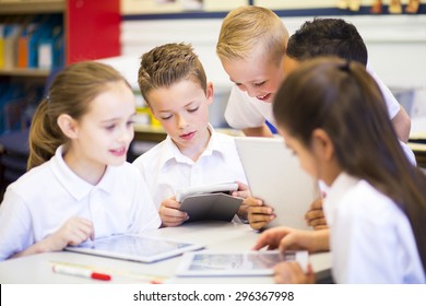 Happy students in classroom using a digital tablet, they are all wearing uniforms. - Powered by Shutterstock