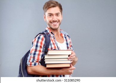 Happy Students Life. Nice Cheerful Young Student Holding Books And Expressing Gladness While Standing Isolated On Gray Background.