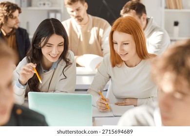 Happy students using laptop in class. Smiling school, college or university student girls sitting at desk in classroom and looking at laptop computer. Technology in education concept