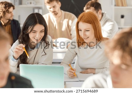 Happy students using laptop in class. Smiling school, college or university student girls sitting at desk in classroom and looking at laptop computer. Technology in education concept
