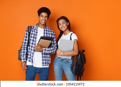 Happy students wearing backpacks and holding exercise books, orange background