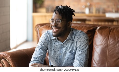 Happy Stylish Afro American Hipster Guy Portrait. Young Black Man, Student, Self Employed Business Owner With Trendy Haircut, Glasses, Toothy Smile Sitting On Leather Sofa At Home. Banner, Head Shot