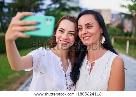 Happy stylish attractive smiling daughter with mother take selfie photo portrait on phone camera while walking together outdoors 