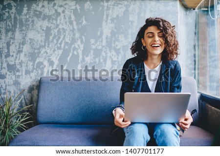 Happy stylish female blogger laughing while chatting with friends in social networks on laptop device using wireless internet in coworking.Positive young woman doing shopping online on website