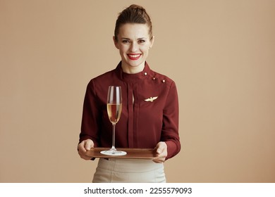 happy stylish flight attendant woman against beige background with a glass of champagne. - Shutterstock ID 2255579093