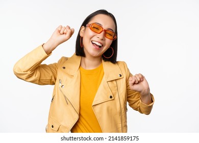 Happy stylish korean girl in sunglasses, dancing and laughing, smiling carefree, standing over white background - Shutterstock ID 2141859175
