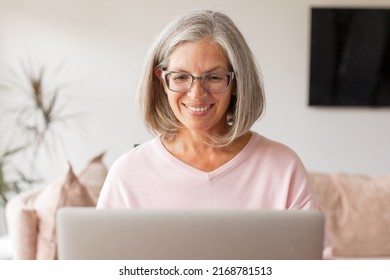 Happy Stylish Mature Old Woman Remote Working From Home Distance Office On Laptop Taking Notes. Smiling 50s Middle Aged Business Lady Using Computer Watching Webinar Or Chatting