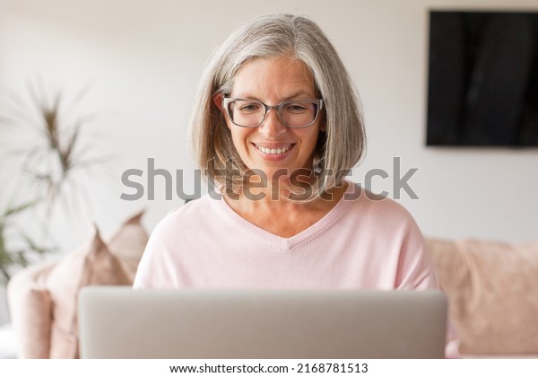 Happy stylish\
mature old woman remote working from home distance office on laptop\
taking notes. Smiling 50s middle aged business lady using computer\
watching webinar or\
chatting