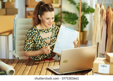 Happy Stylish Middle Aged Small Business Owner Woman With Clipboard Video Chatting On Laptop In The Office.