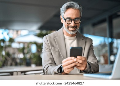 Happy stylish older busy businessman investor holding smartphone looking at cellphone doing banking payments. Middle aged business man using mobile cell phone working outdoors. Candid photo. - Powered by Shutterstock