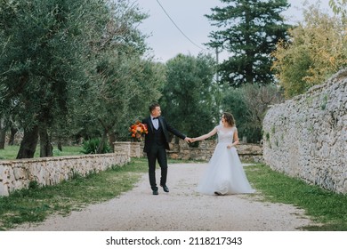 Happy stylish smiling couple walking in Tuscany, Italy on their wedding day. The bride and groom walk down the street by the hands. A stylish young couple walks. Husband and wife communicate nicely