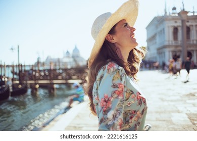 happy stylish tourist woman in floral dress with hat sightseeing on embankment in Venice, Italy.